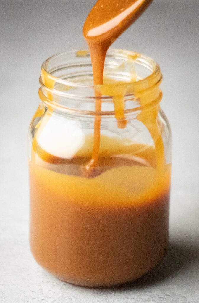 Caramel sauce dripping from spoon into a jar