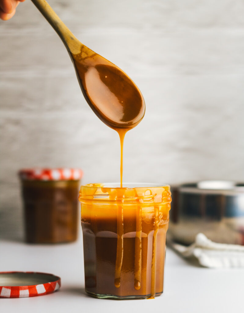 Caramel sauce dripping from wooden spoon into jar 