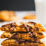 Close up of halved chocolate chiop cookies with whole cookies and milk in the rear