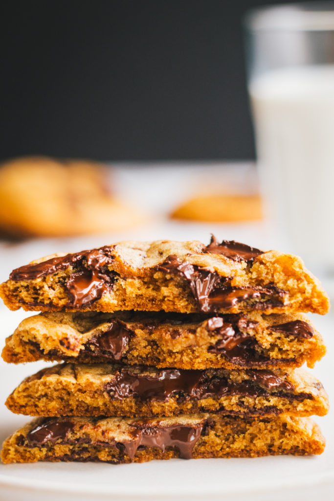 Close up of halved chocolate chiop cookies with whole cookies and milk in the rear