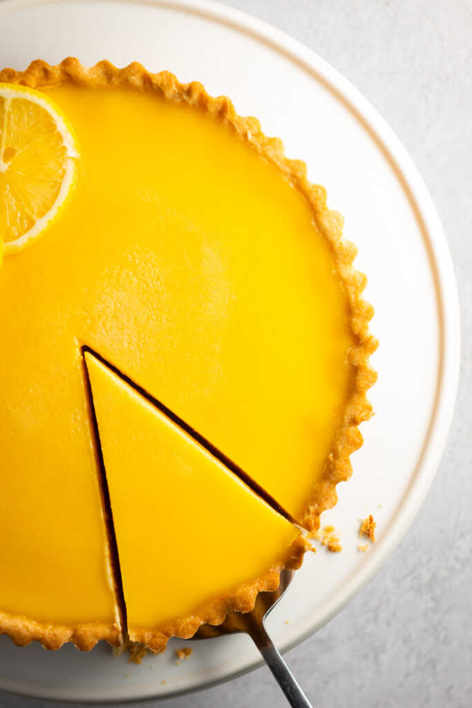 Overhead view of a no-bake lemon curd tart with one slice cut out, showing glossy yellow curd and golden crust.