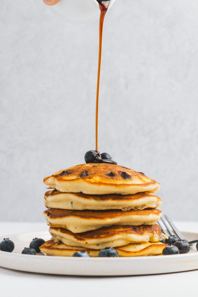 Stack of Blueberry Pancakes being drizzled with maple syrup