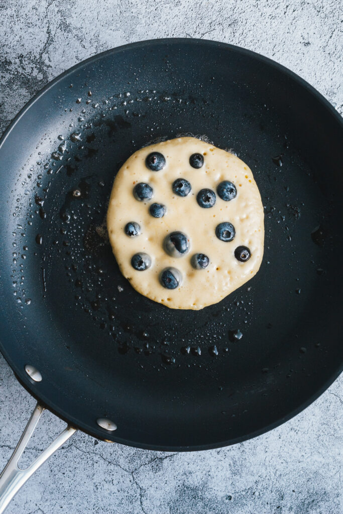 Pancake batter in frying pan topped with blueberries