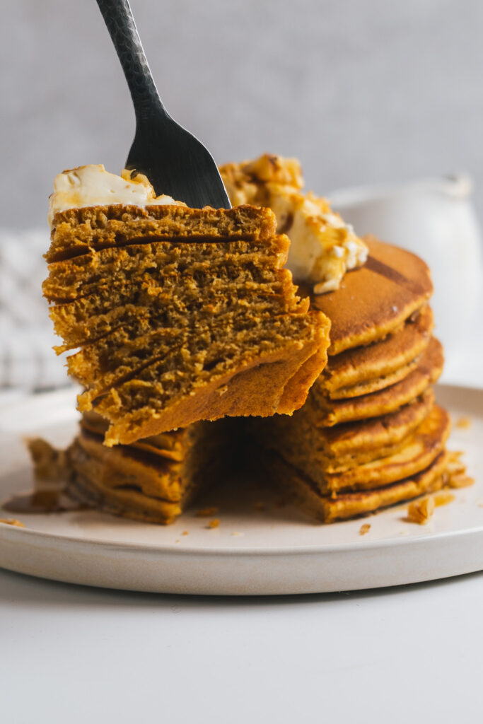 Forkful of carrot cake pancakes with stack of pancakes in the rear