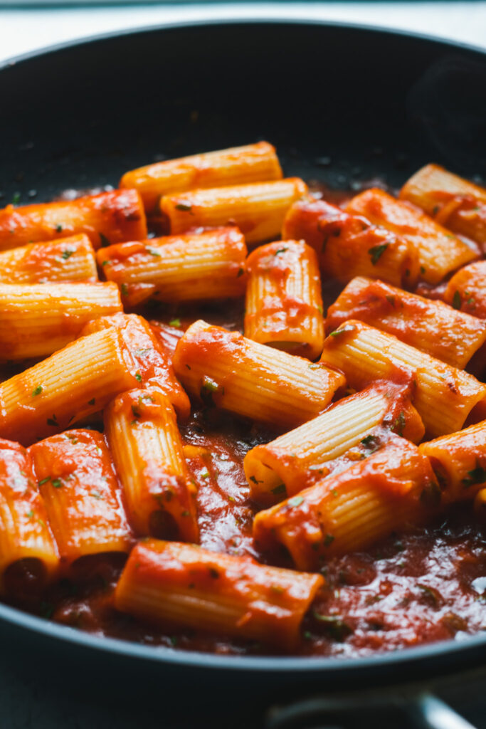 Rigatoni tossed in tomato sauce in a frying pan