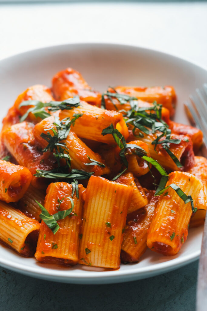 Rigatoni tossed in a tomato sauce topped with basil in a bowl
