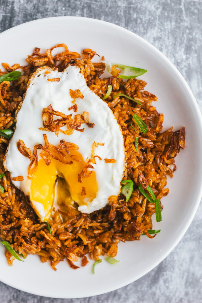 nasi goreng kampung in a bowl with a fried egg cut open with a runny yolk