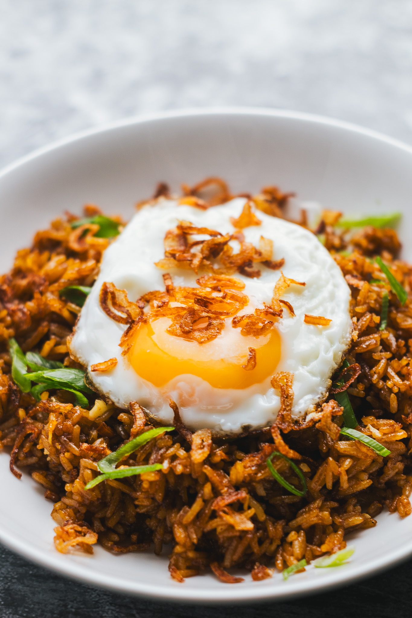 Spicy fried rice topped with a fried egg and crispy shallots in a bowl