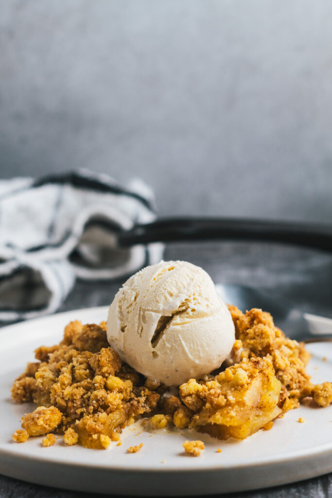 Apple Crisp topped with vanilla ice cream on a plate