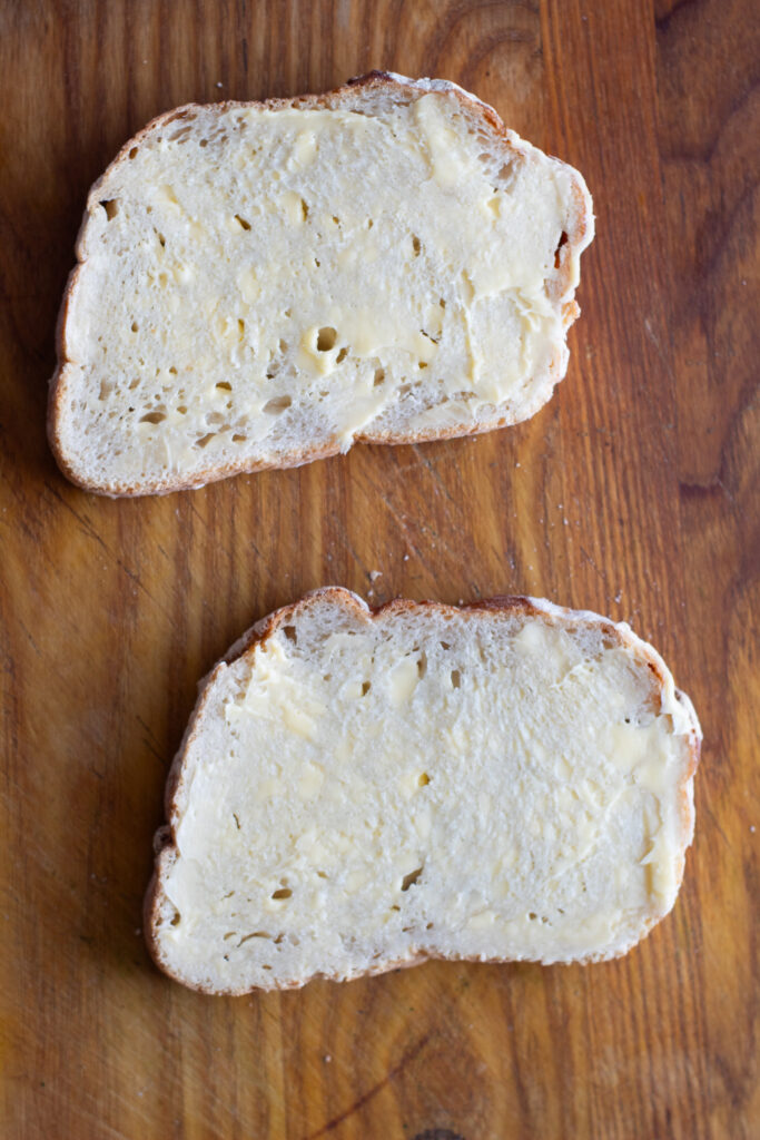 Buttered slices of sourdough bread on a chopping board