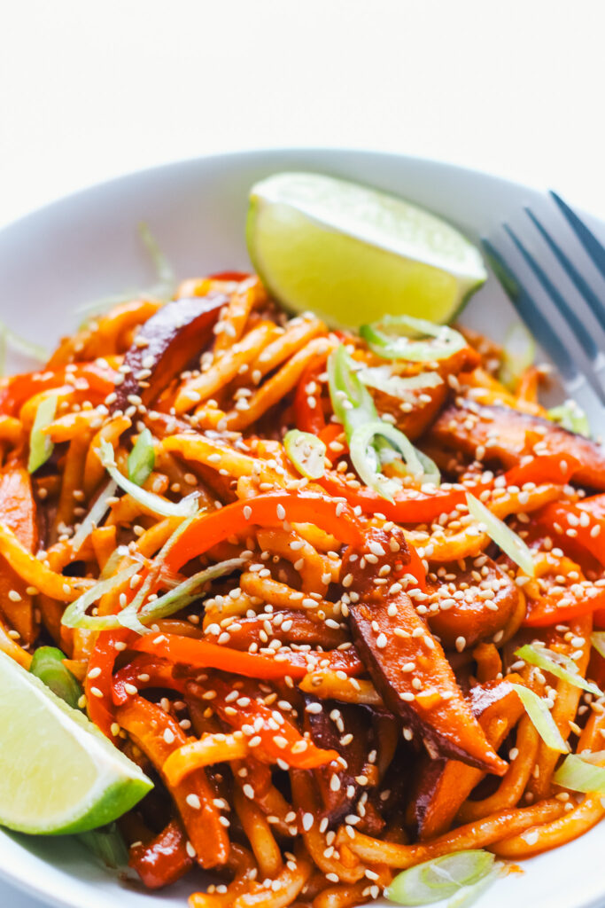 Gochujang noodles in a bowl with a fork and lime segments