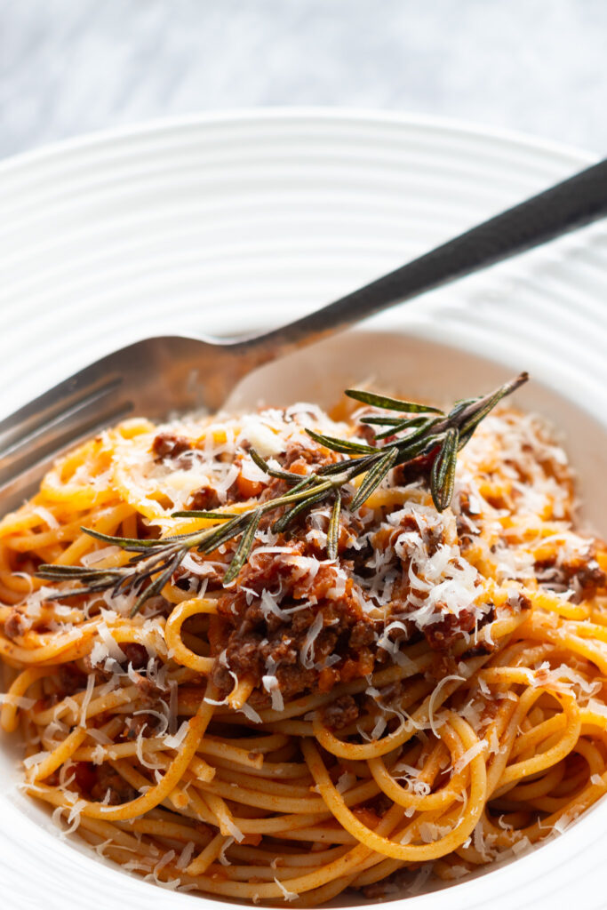 Spaghetti bolognese topped with fried rosemary