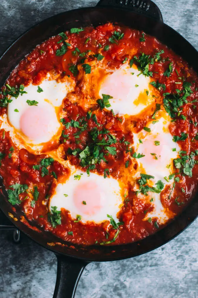 Moroccan Shakshuka with poached eggs simmered in a rich rose-harissa tomato sauce in a cast iron skillet.
