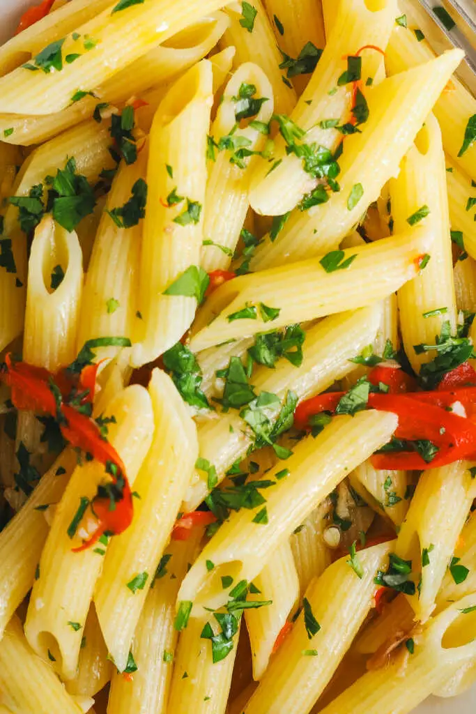 Close-up of Penne Aglio e Olio with glossy olive oil, sliced garlic, red chilli and fresh parsley