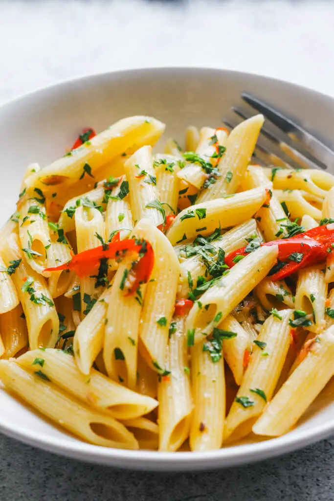 Penne Aglio e Olio served in a white bowl, garnished with parsley and sliced red chilli