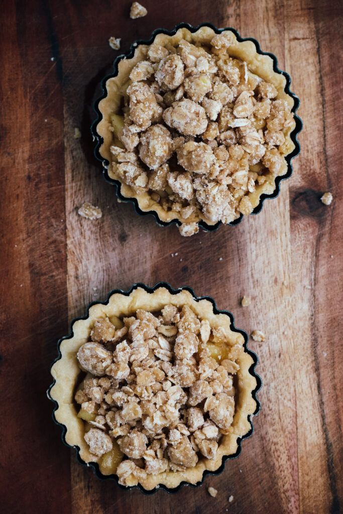 Apple crumble tart shells filled with apples and topped with crumble, ready for cooking
