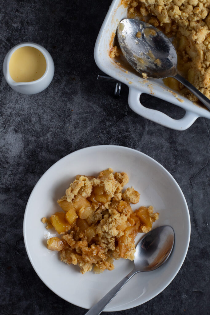 Apple crumble in a bowl with custard in a jug