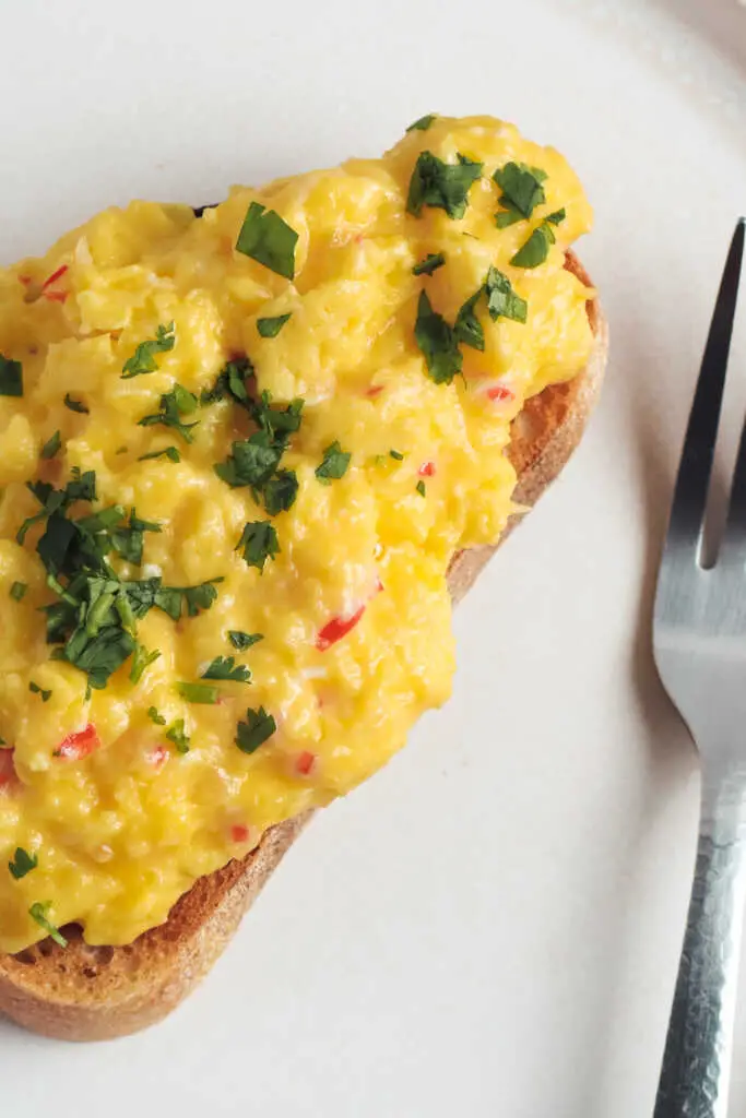 Overhead view of chilli scrambled eggs topped with herbs on a slice of toast.