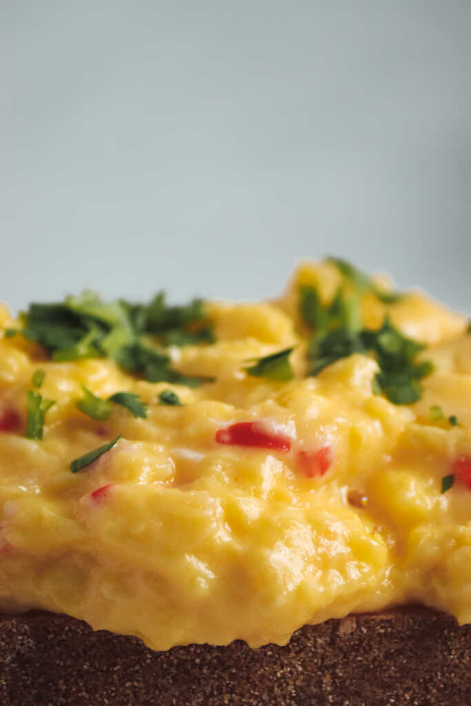 Creamy scrambled eggs with red chilli and herbs on toast, close-up shot.