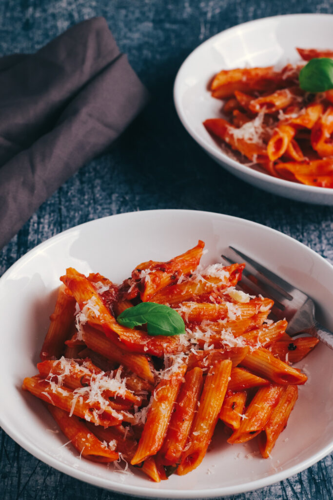 two bowls of Penne Napoli topped with parmesan and basil