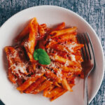 Bowl of Penne Napoli topped with parmesan and basil