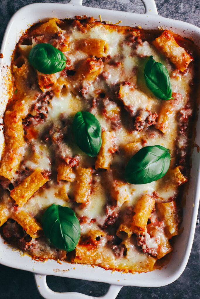 Baked rigatoni al forno in a baking dish topped with fresh basil leaves