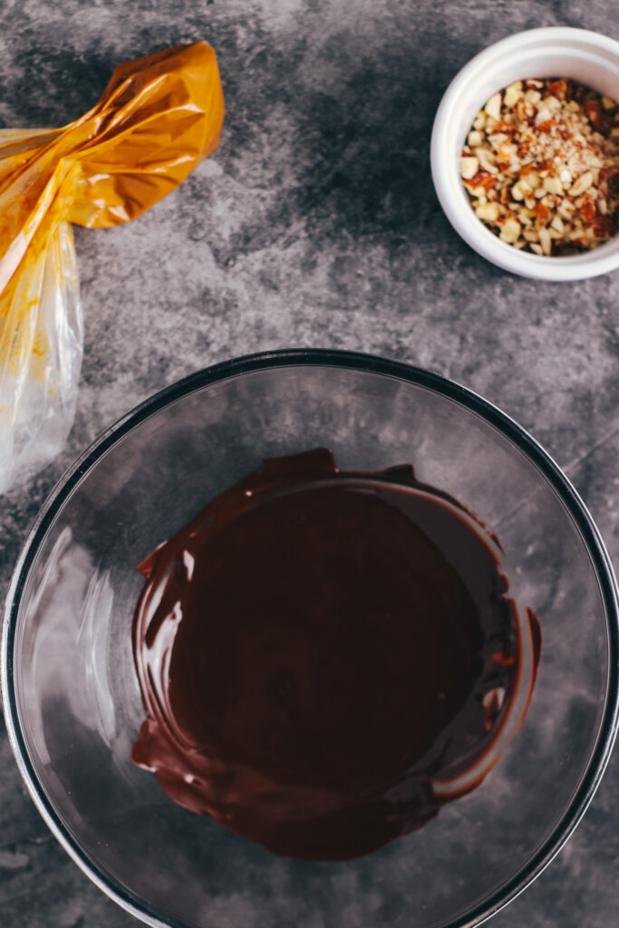 Melted chocolate, peanut butter in a piping bag and chopped almonds on a table