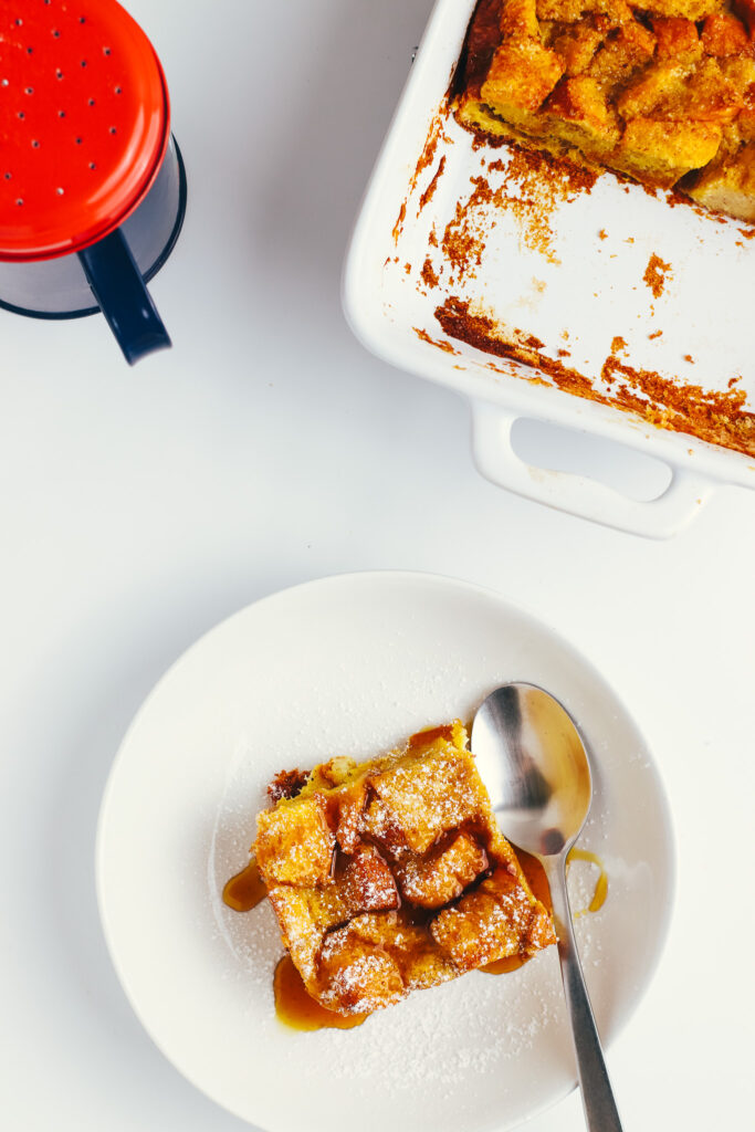 French toast brioche casserole in a bowl topped with icing sugar and maple syrup