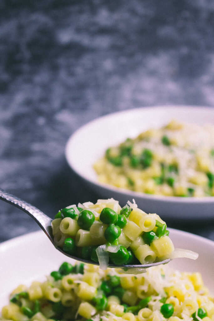 A spoonful of Italian Pasta and Peas with a bowl in the background