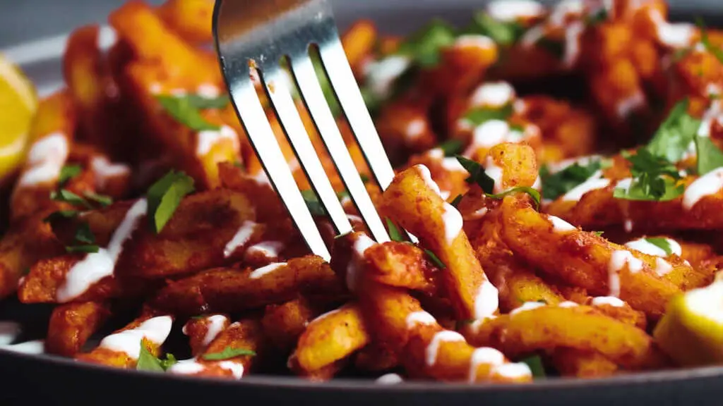 Fork lifting saucy masala fries coated in spicy tomato masala
