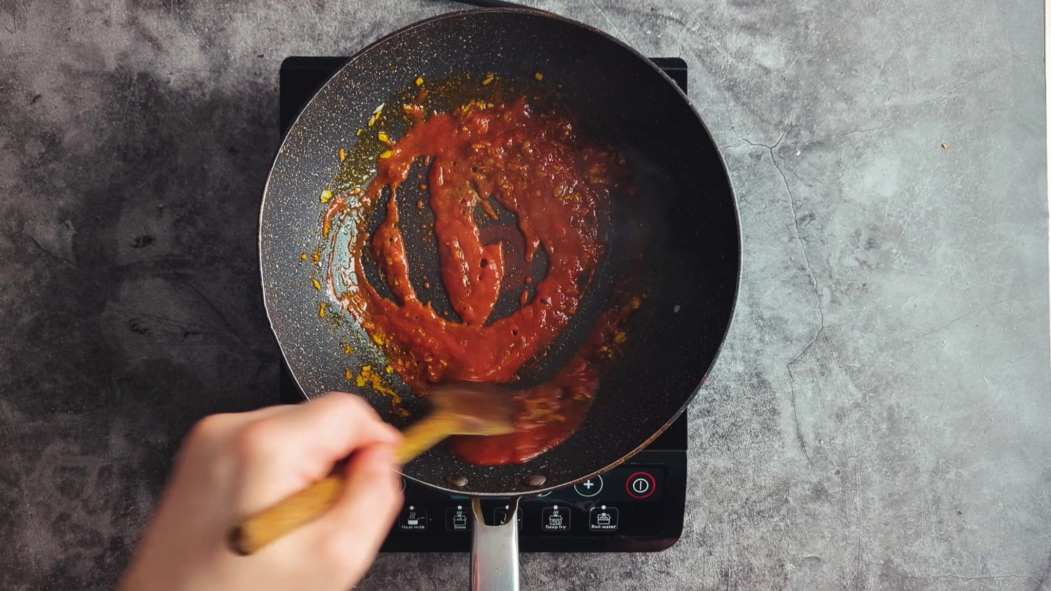 Stirring thick tomato masala sauce in a frying pan with a wooden spoon
