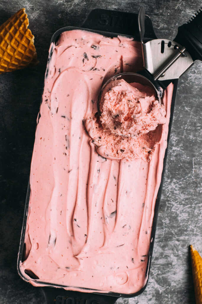 Raspberry chocolate ice cream with an ice cream scoop, surrounded by ice cream cones