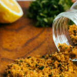 A jar of pangrattato breadcrumbs on a chopping board with lemon and parsley