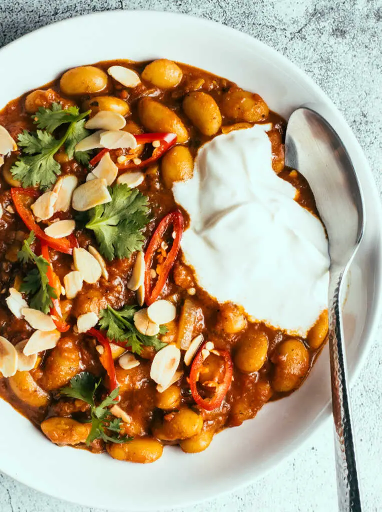 Butter beans curry in a bowl with yoghurt and herbs on top