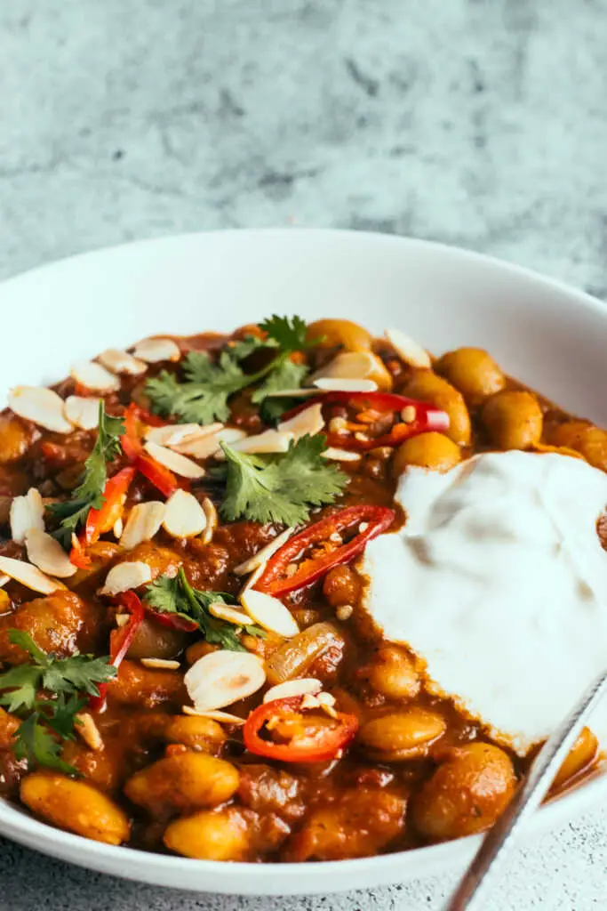 Butter beans curry in a bowl with yoghurt, spoon and herbs