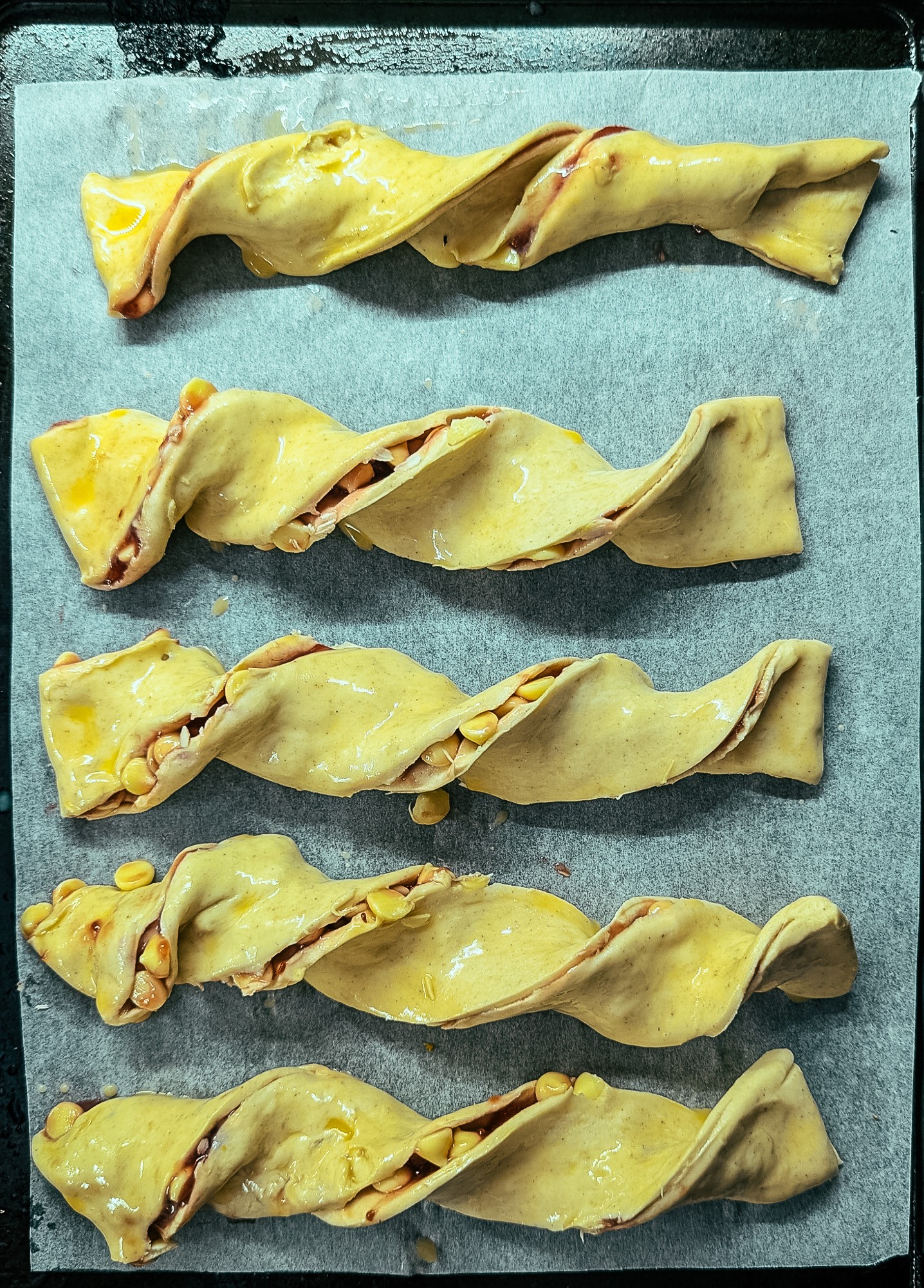 Unbaked raspberry and white chocolate twists on a baking tray, ready to go in the oven.