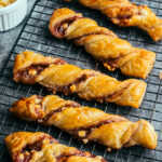 Raspberry and white chocolate torsades cooling on a wire rack, with white chocolate chips in a ramekin.
