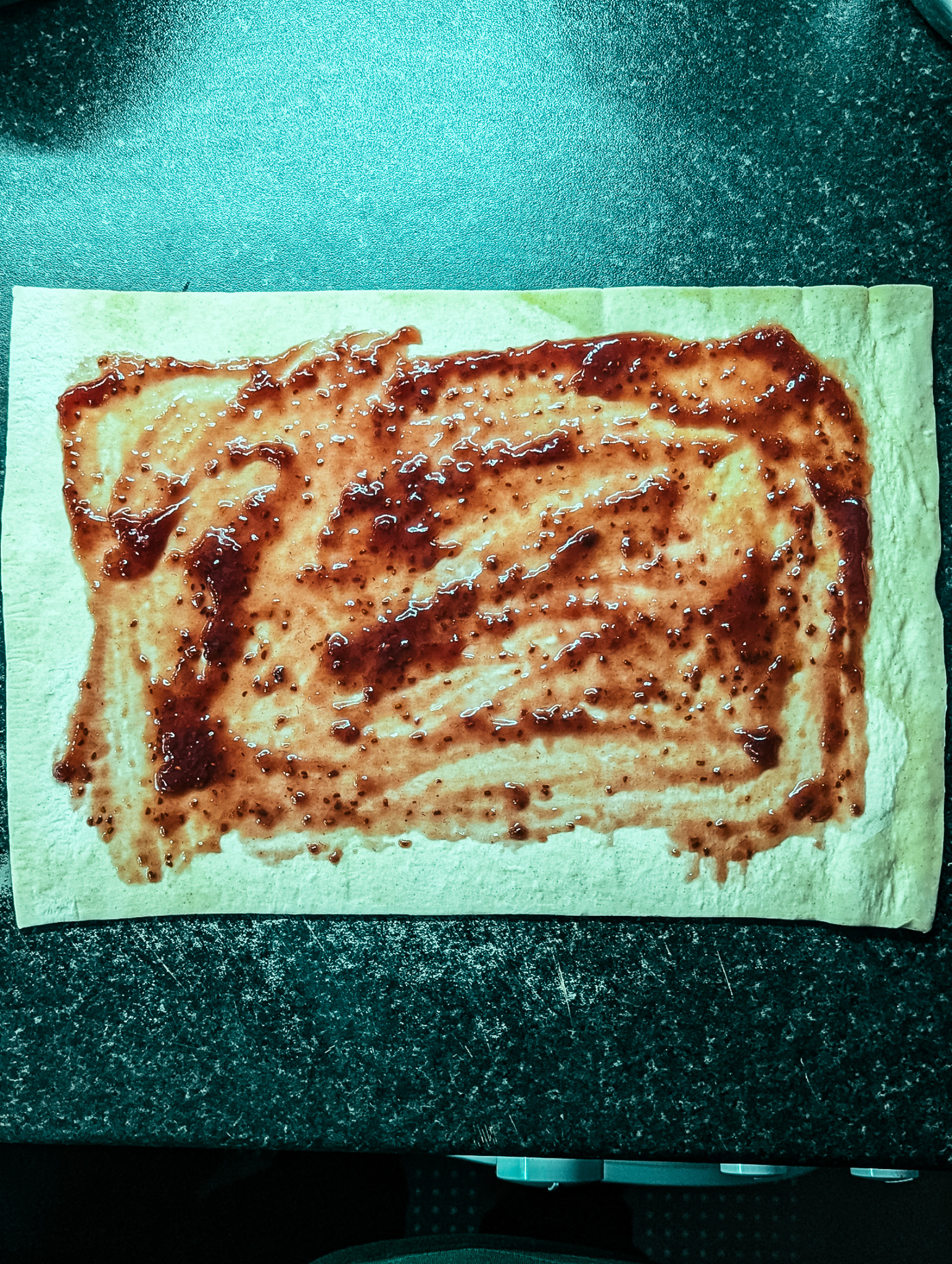 Puff pastry sheet spread with raspberry jam, ready to be filled for homemade chocolate twists.