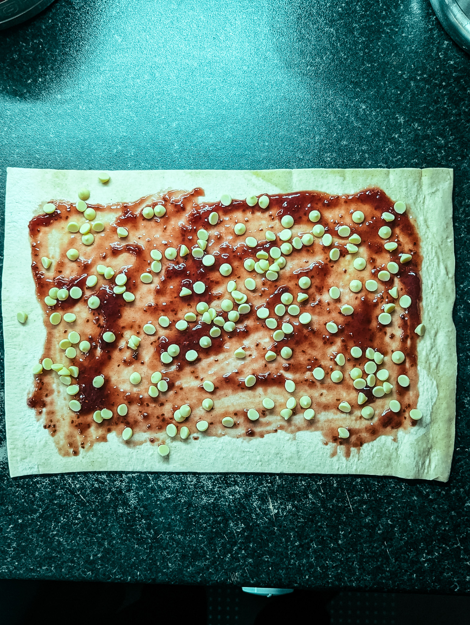 Puff pastry topped with raspberry jam and white chocolate chips, ready to be twisted into chocolate twists.