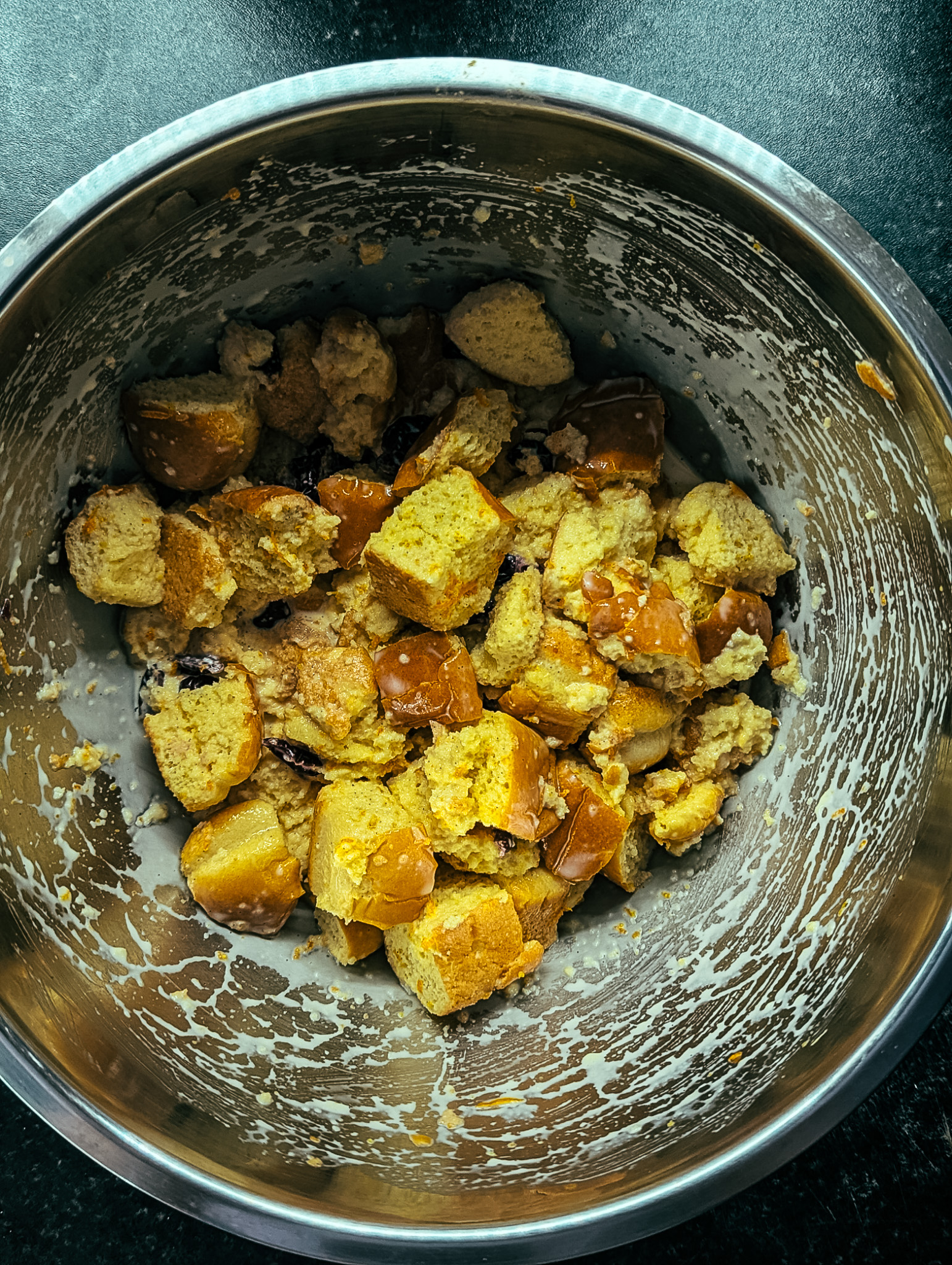 Cubes of brioche bread soaking in custard mixture with cranberries in a mixing bowl