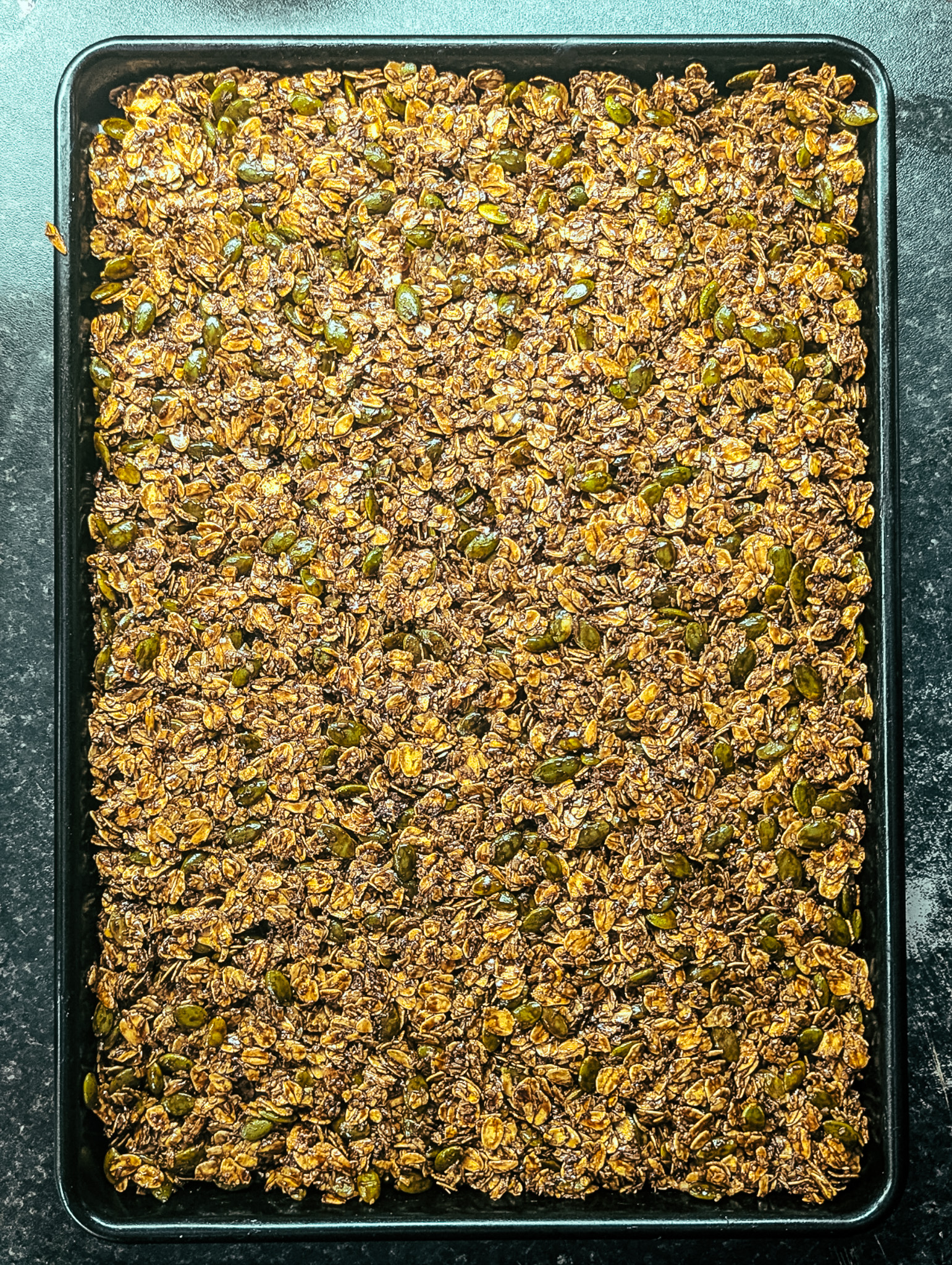 Evenly spread mocha nut free granola on a baking sheet before baking.