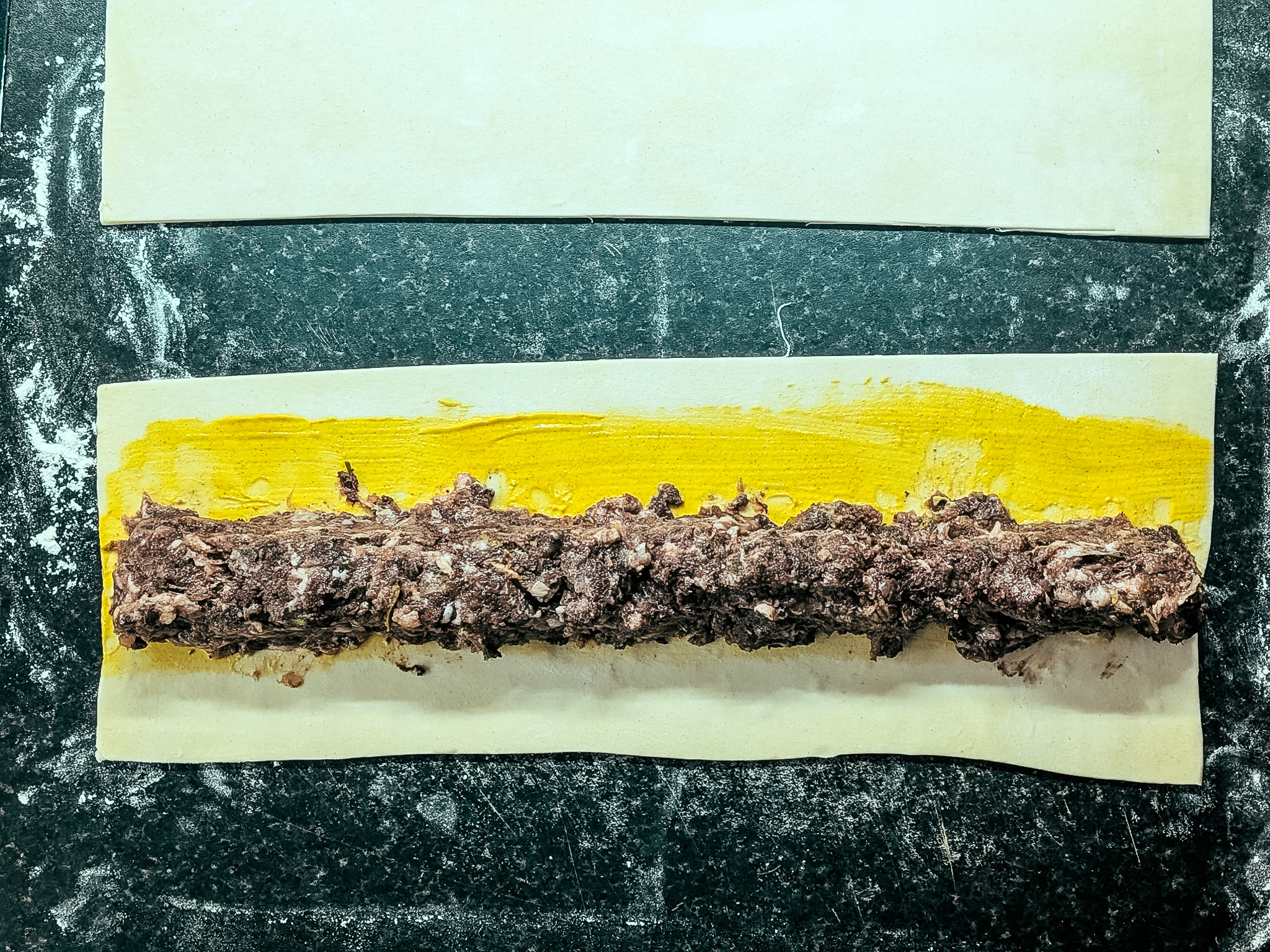 Black pudding sausage mixture placed on mustard-brushed pastry