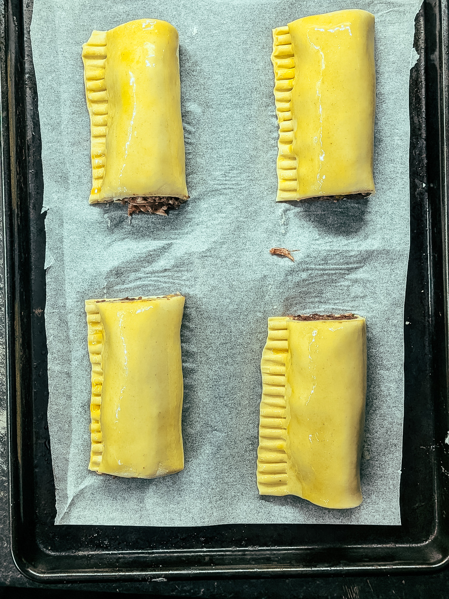 Unbaked sausage rolls on baking tray lined with parchment