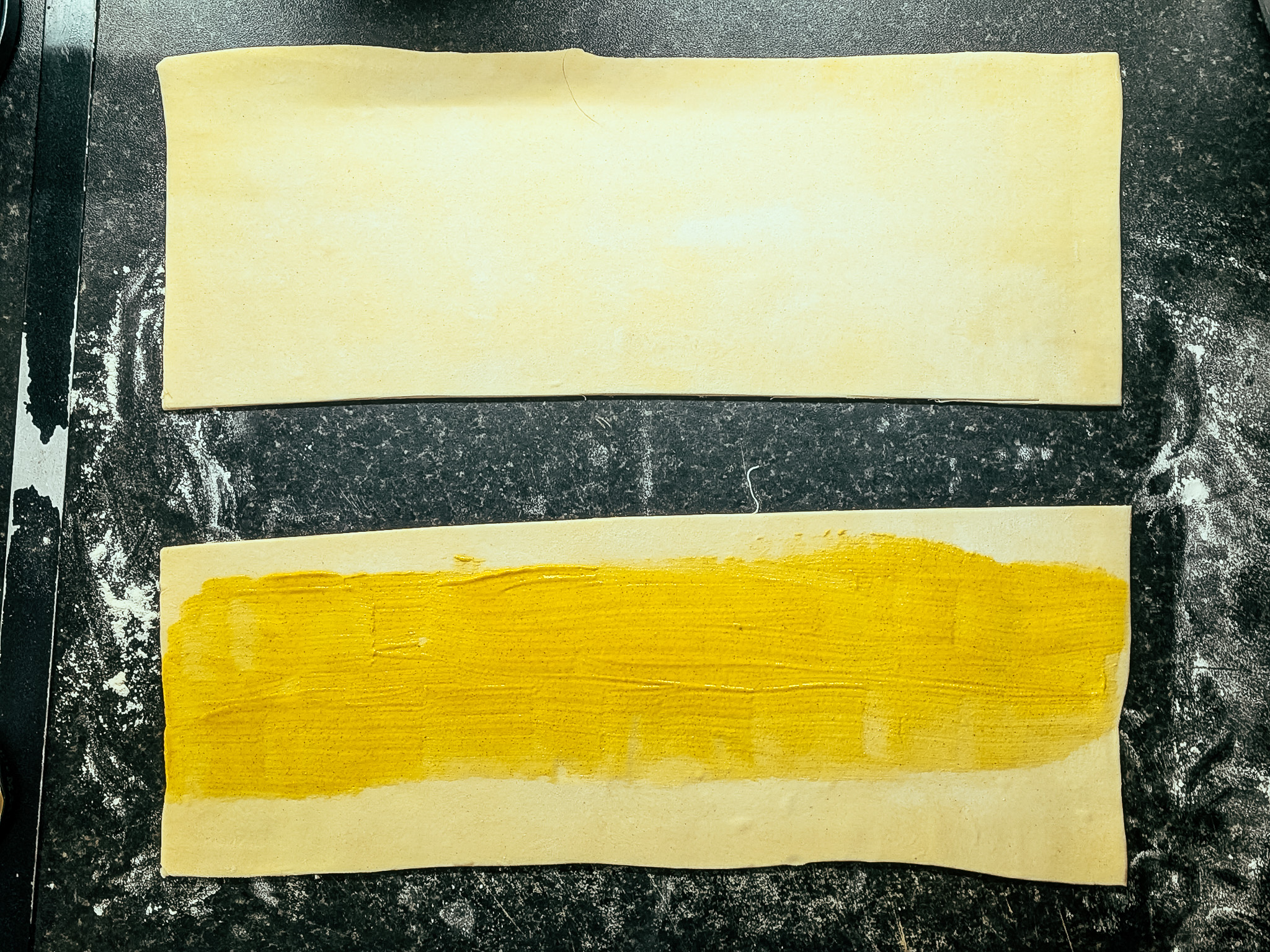 Puff pastry strips brushed with mustard on dark work surface