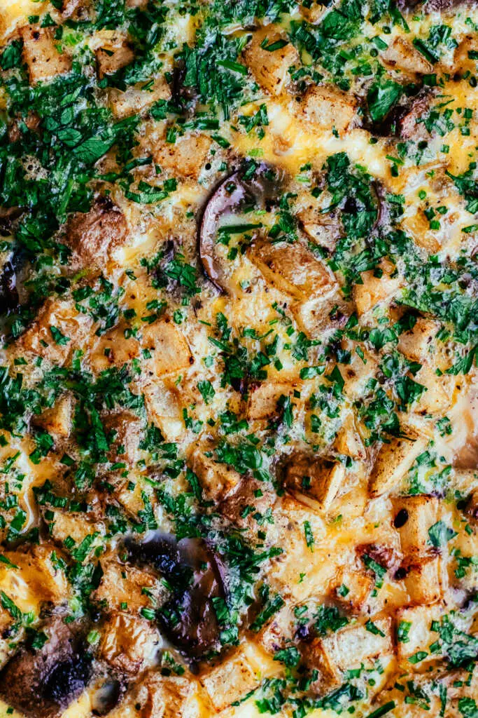 Close-up texture of a golden country omelette with crispy potatoes, bacon, and herbs