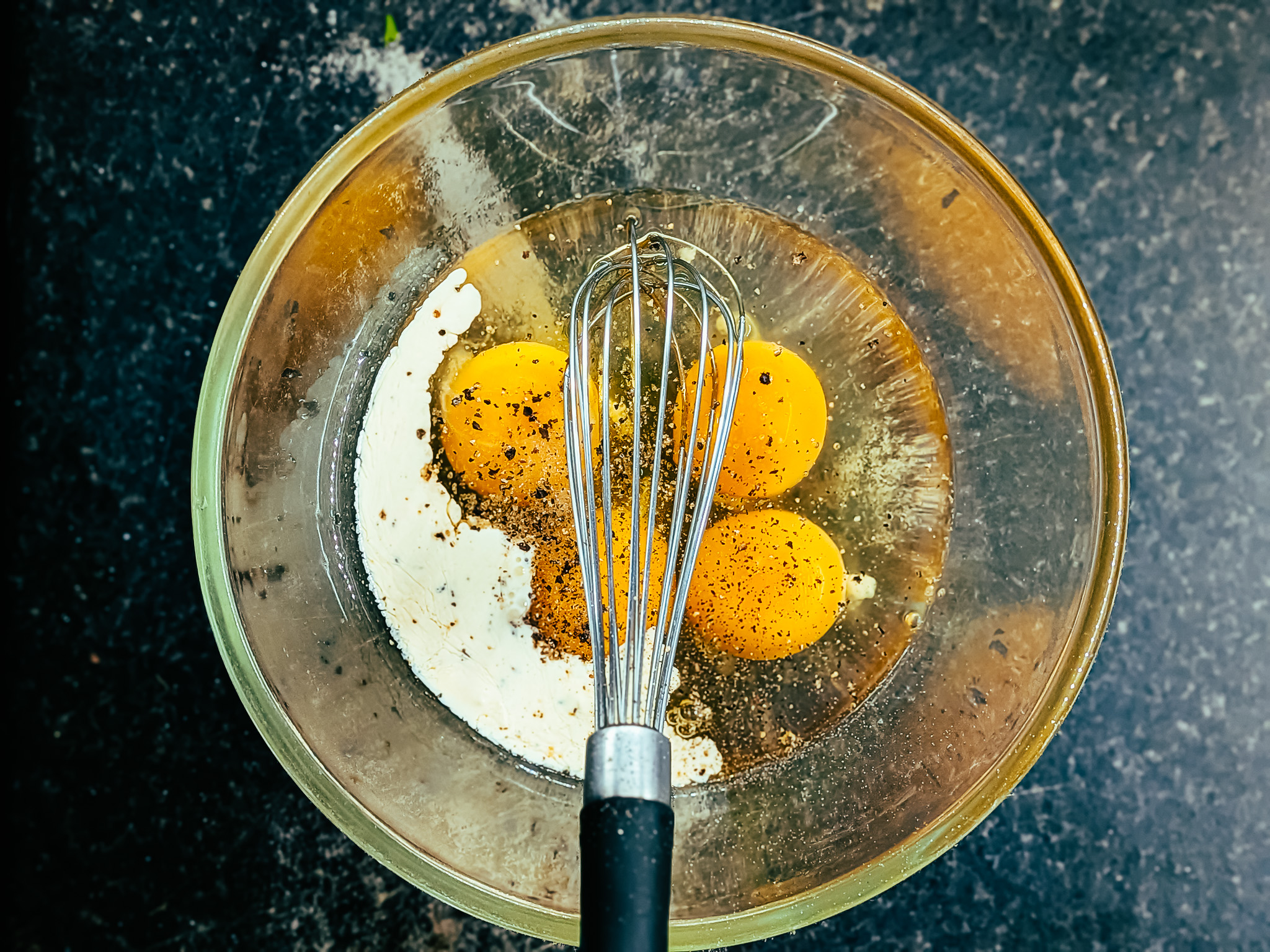 Eggs, cream, salt, and pepper in a glass bowl with a whisk, ready for making a rustic country omelette