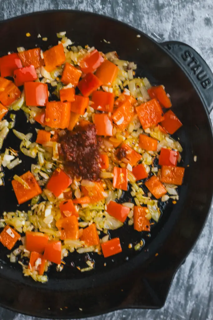 Rose harissa added to sautéed onions and peppers in a cast iron pan to build the warm, spiced flavour of Moroccan Shakshuka.