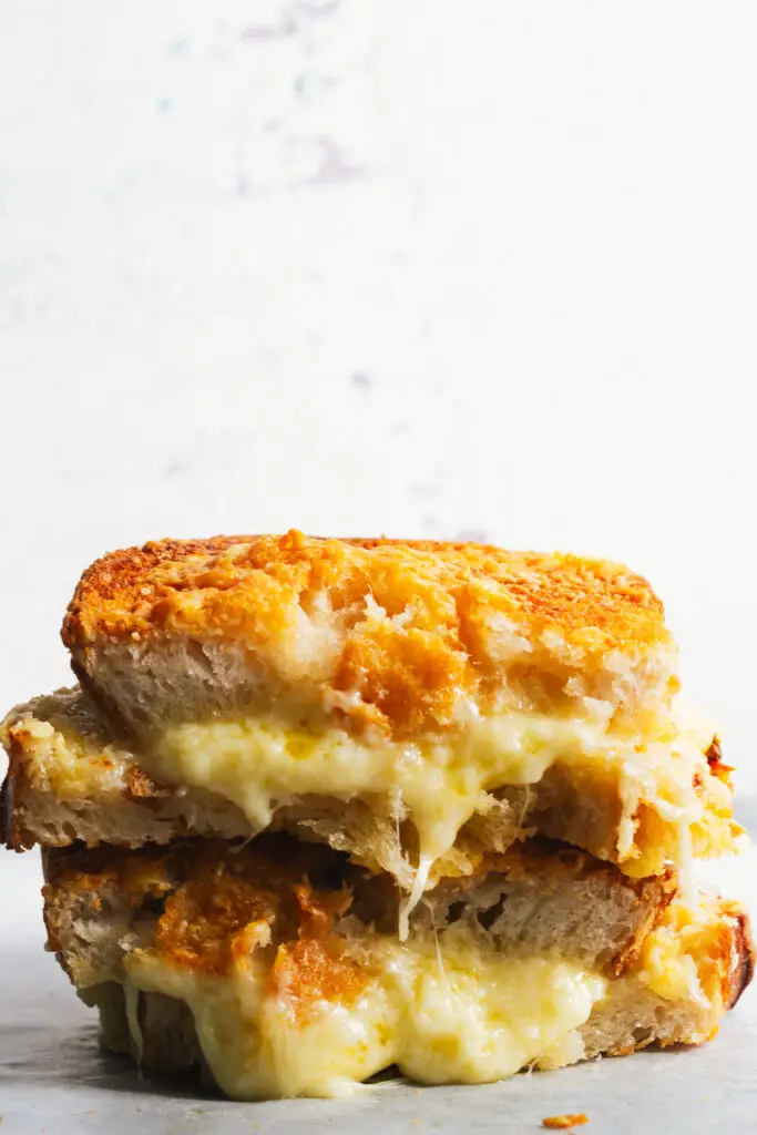 A stack of sourdough grilled cheese sandwiches showing melted cheese oozing from the centre.