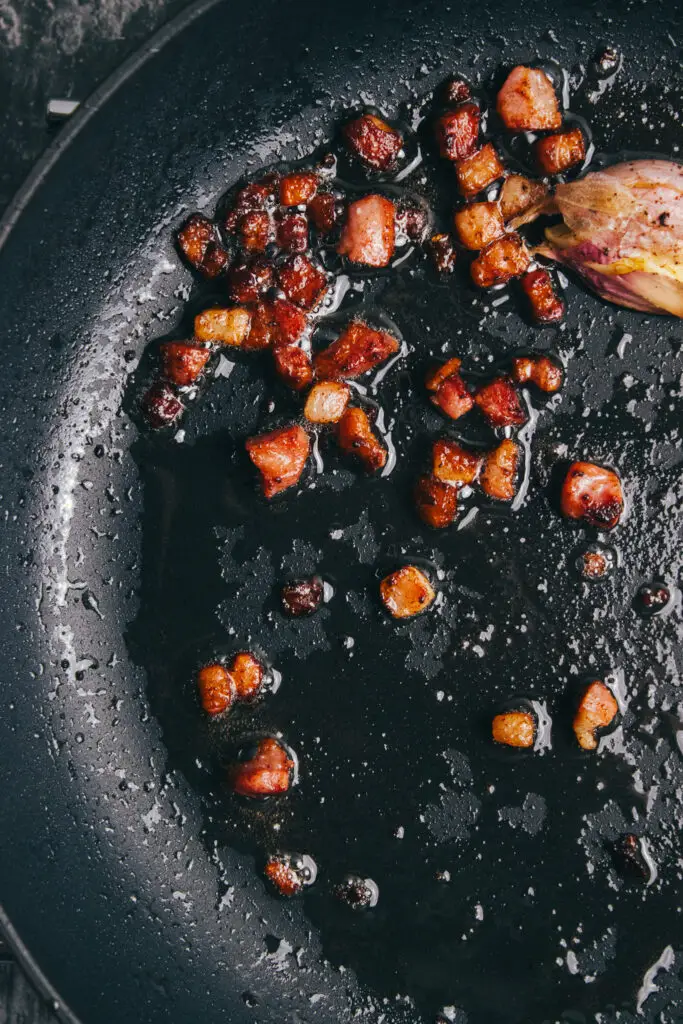 Crispy pancetta pieces frying in a pan for carbonara