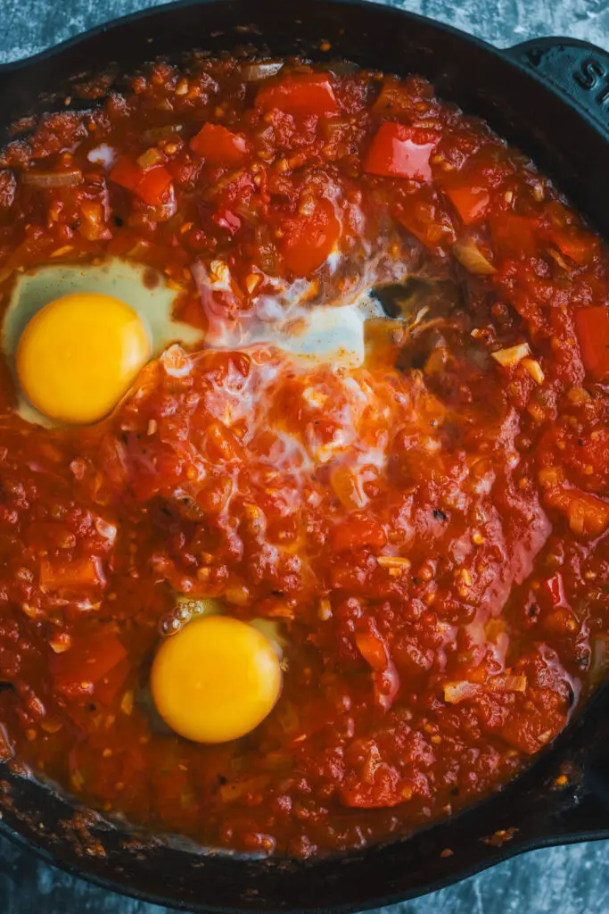 Raw eggs cracked into wells in a thick, spiced tomato and pepper sauce for Moroccan Shakshuka.